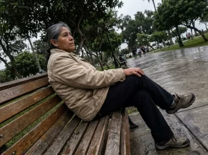 mujer mayor sentada en una banca de un parque con la mano sobre la rodilla por dolor de artritis y artrosis
